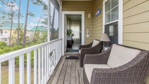 A porch with wicker furniture and a ceiling fan, leading to a room with a view of neighboring houses and trees. - Coastal Tranquility: Beautiful Condo Offering Poolside Serenity Near Beach (Pensacola)