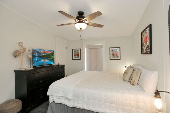 A bedroom with a bed, a ceiling fan, a TV, and artwork on the walls. - Flirty Flamingo Fun in the Sun, Near SJB Park a Killer Spot for Sunsets (St. Joe Beach)