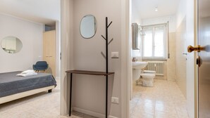 A bedroom with a bed, a chair, a coat rack, and a bathroom with a toilet and sink. - Residence Bonomelli apt. no. 15 studio apartment (Bergamo)