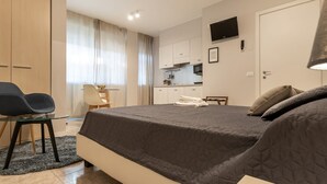 A modern bedroom with a large bed, a desk, and a kitchenette in the background. - Residence Bonomelli apt. no. 15 studio apartment (Bergamo)