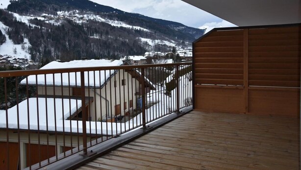 Una terraza de madera con baranda metálica que da a un paisaje montañoso nevado.