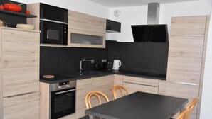 Una cocina moderna con armarios de madera, encimera negra, microondas integrado, estufa y un comedor con mesa y sillas.