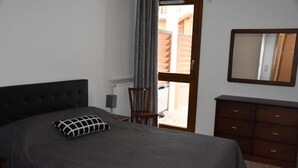 Un dormitorio con cama, una silla, un aparador y una ventana con cortinas.