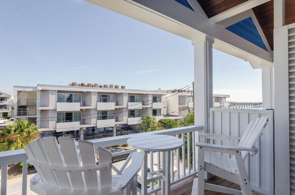 Ein Balkon mit weißen Stühlen und einem kleinen Tisch, mit Blick auf ein modernes Gebäude mit mehreren Balkonen und blauem Himmel.