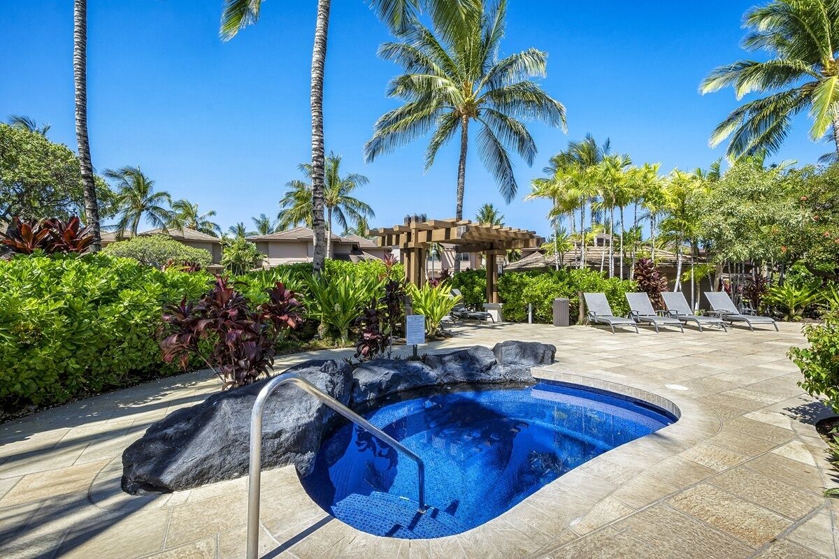 A pool area with a clear blue pool, lounge chairs, palm trees, and a pergola.