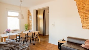 Un salon moderne avec un canapé, un coin repas comprenant des chaises et une table, une grande fenêtre et un mur en briques.