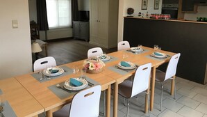 A dining area with a long table set for four, white chairs, and a kitchen area with cabinets and a countertop. - Cozy Vacation Home for 8 Persons in Heers (Heers)