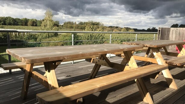 A wooden picnic table on a deck with a metal railing and a grassy field in the background. - Cozy Vacation Home for 8 Persons in Heers (Heers)