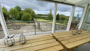 Une table en bois avec des chandeliers en métal, une rambarde en verre et une vue sur un parc avec des arbres et une aire de jeux.