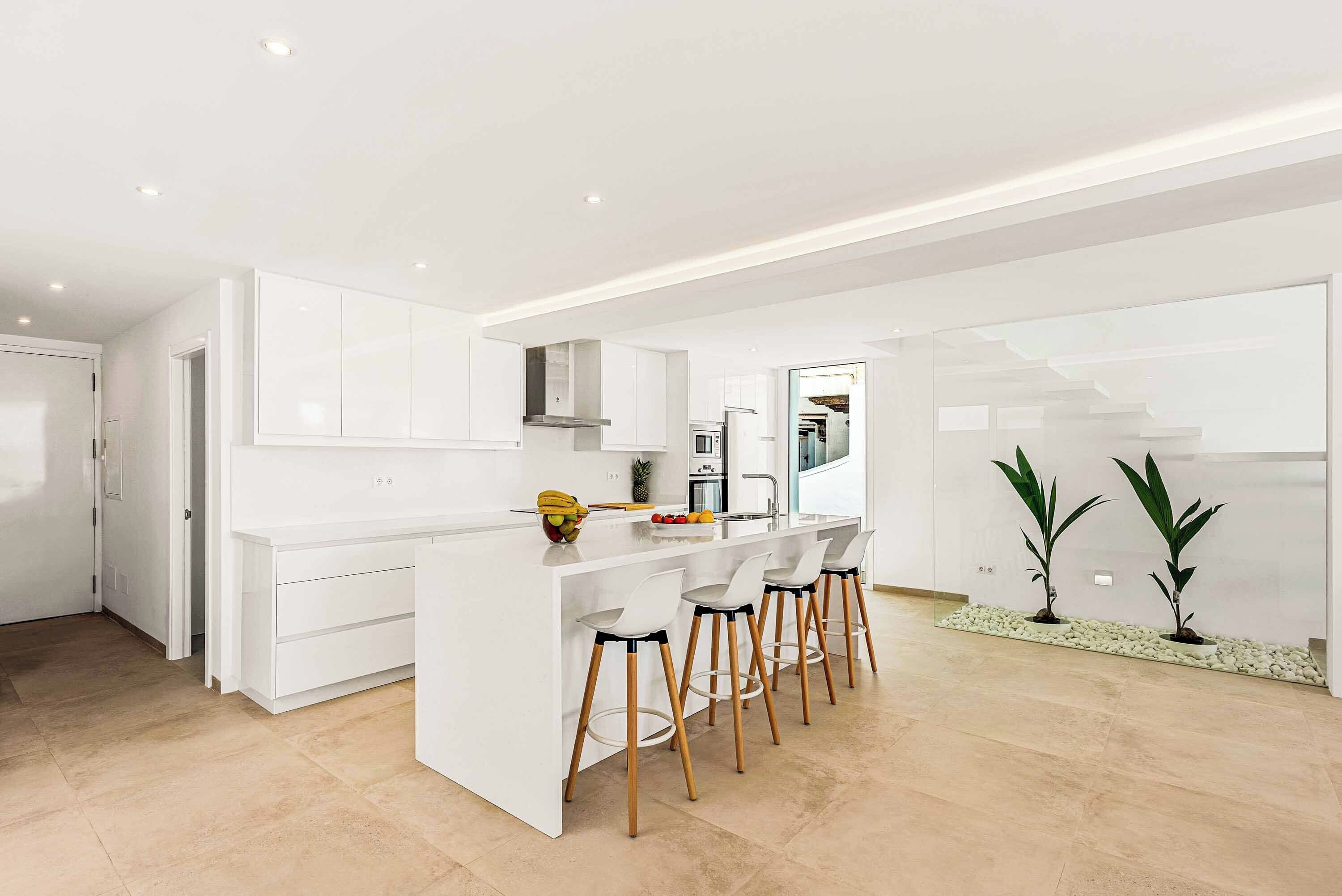 Une cuisine moderne avec des meubles blancs, un îlot central doté de tabourets de bar et un escalier menant à un autre niveau.