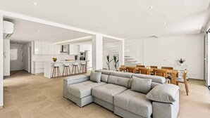 A modern living room with a sectional sofa, a dining area with wooden chairs, and a kitchen in the background.