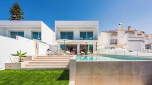 A modern two-story house with a swimming pool, outdoor seating, and a well-maintained lawn.