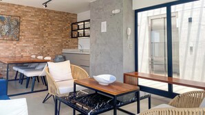 Une cuisine moderne avec un mur de fond en briques, un coin repas avec des chaises et une table, et une grande porte-fenêtre coulissante donnant sur un balcon.