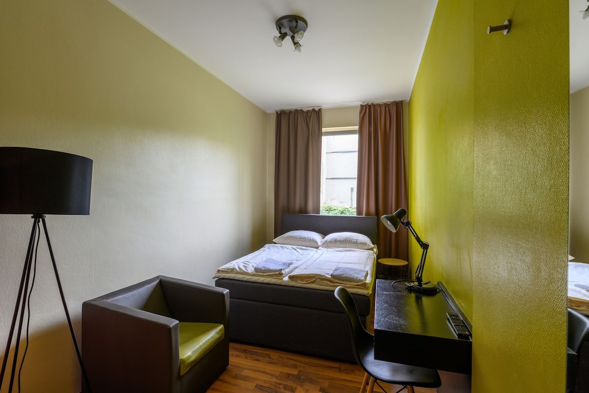 Een hotelkamer met een bed, bureau, stoel, lamp en een raam met gordijnen.