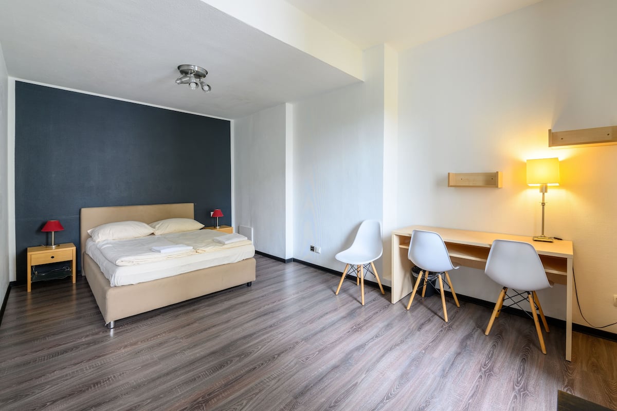 Een moderne hotelkamer met een bed, bureau, twee stoelen, een lamp en een nachtkastje.