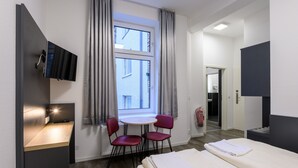A hotel room with a bed, a desk with a computer, a TV mounted on the wall, and a window with curtains.