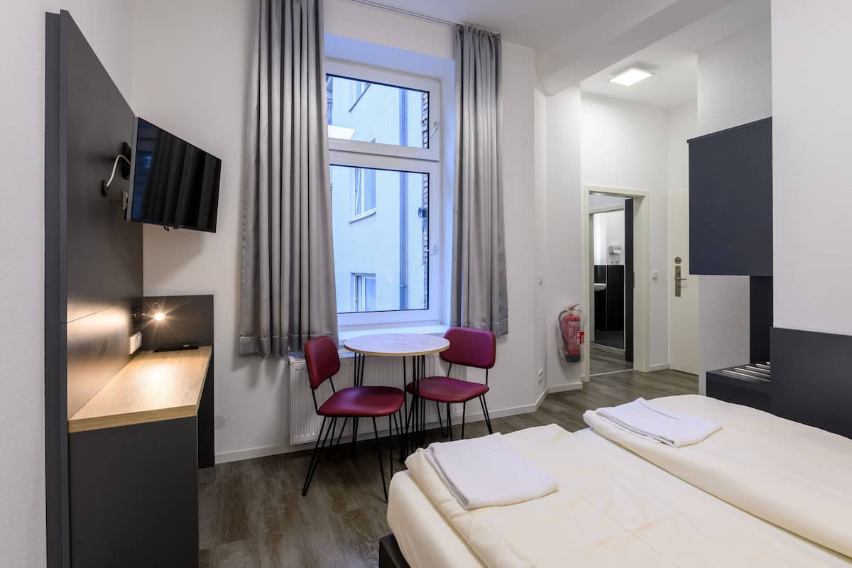 Een hotelkamer met een bed, een bureau met een computer, een aan de muur bevestigde televisie en een raam met gordijnen.