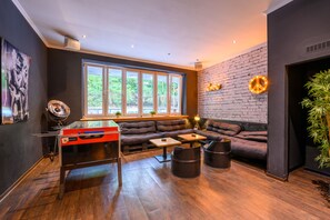 A modern lounge with a foosball table, a large window, a brick wall, and a cozy seating area. - Sonata City Hotel (Cologne)
