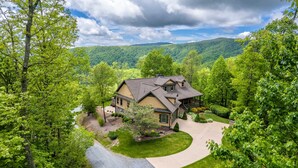 A two-story house with a large front yard, surrounded by dense trees and a mountain backdrop. - Heaven South-Mountain Views - Hot Tub - Fire Pit -Secluded (Bryson City)
