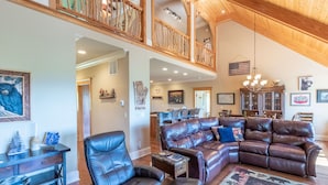 A spacious living area with a leather sofa, a dining table, and a high ceiling with wooden beams. - Heaven South-Mountain Views - Hot Tub - Fire Pit -Secluded (Bryson City)