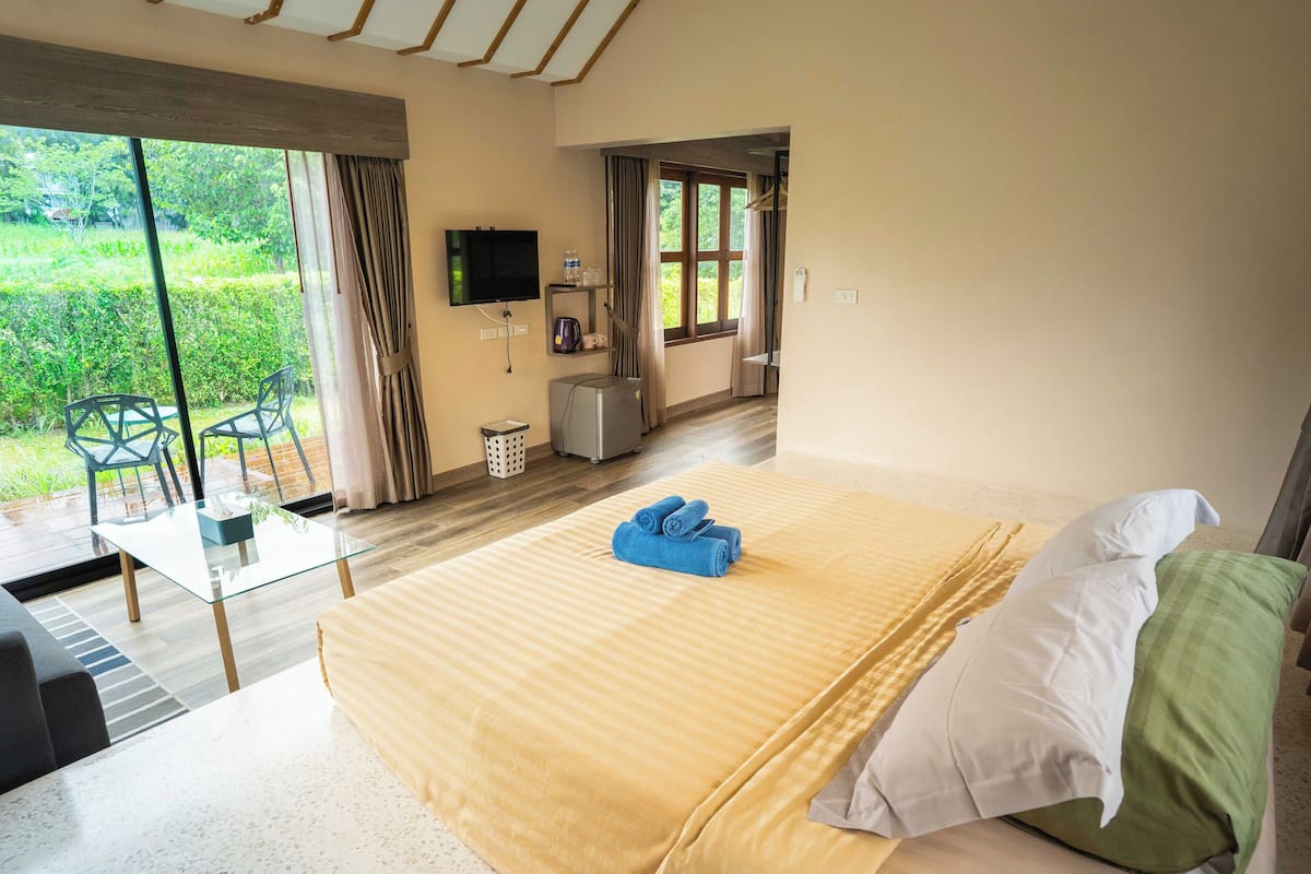A hotel room with a bed, a TV, a small table, and a view of the outdoors.