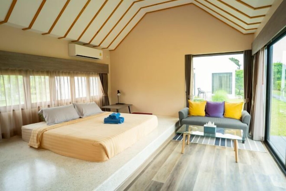 A bedroom with a bed, a sofa, a glass coffee table, and a large window.