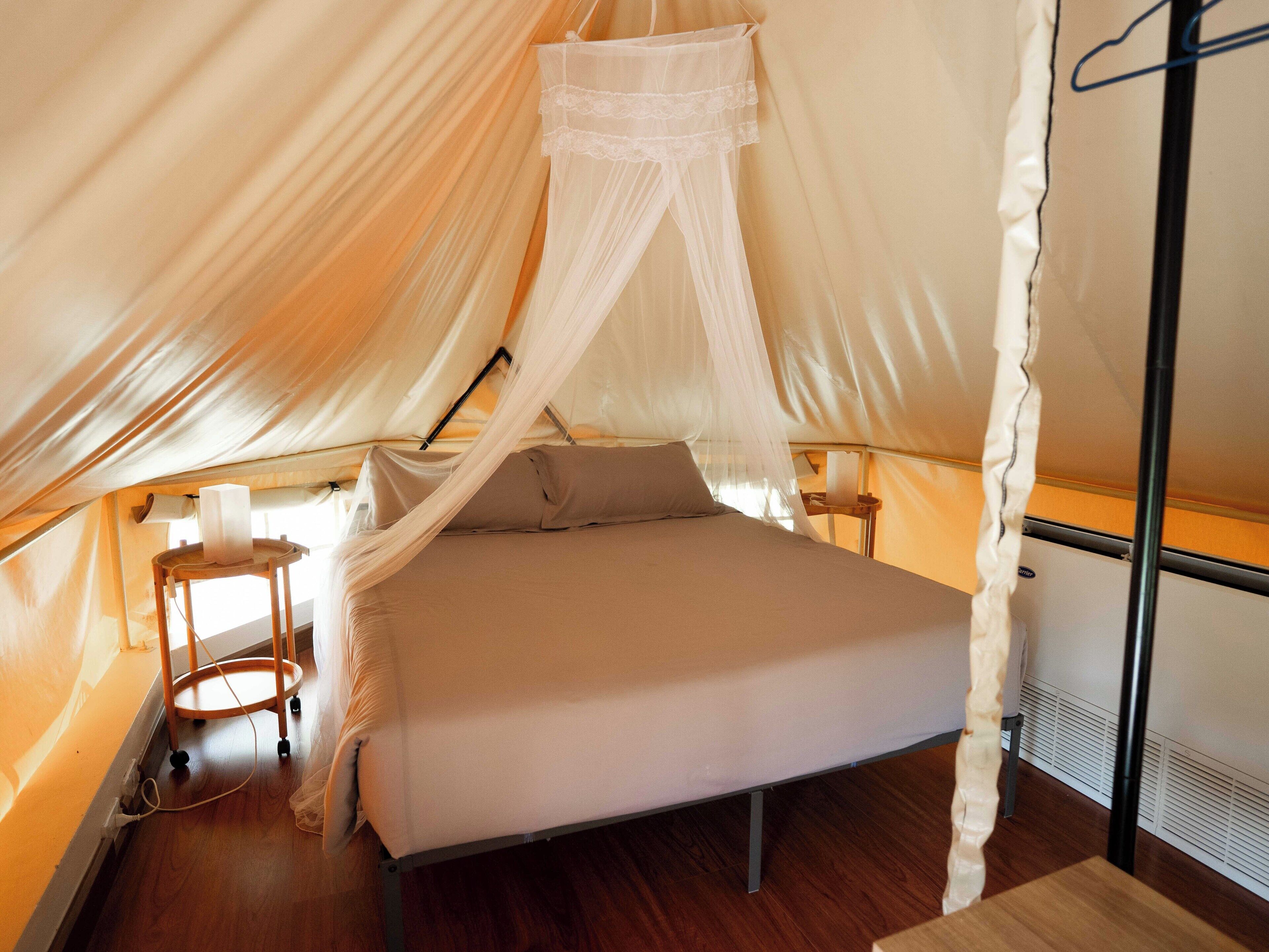 A tent-style room with a bed, mosquito net, and a small table with a lamp.