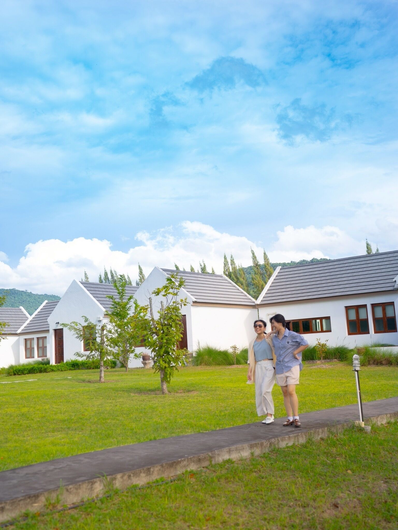 A residential area with white houses, a paved walkway, and a grassy lawn.