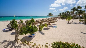 Een strand met rieten parasols, palmbomen en ligbedden.