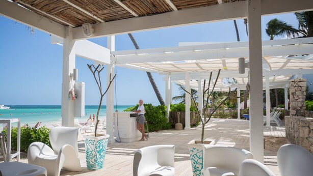 Een terras aan het strand met witte lounge fauteuils, een stenen zuil en uitzicht op de oceaan.