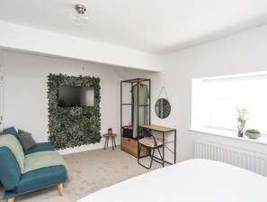 A bedroom with a bed, a desk, a chair, a TV, and a window with a plant. - Y Goedwig (Llanfairpwllgwyngyll)