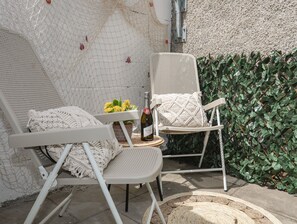 Two white wicker lounge chairs with macrame cushions, a small table with a bottle of wine, and a potted plant with yellow flowers. - Y Goedwig (Llanfairpwllgwyngyll)