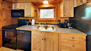 A compact kitchen with wooden cabinets, a double sink, a microwave, a toaster, and a coffee maker. - Sandys Beach House (Hayward)