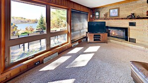 A living room with large windows, a fireplace, and a television. - Sandys Beach House (Hayward)