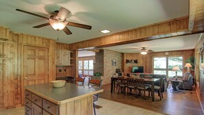 A spacious kitchen with wooden cabinets, a central island, and a dining area with chairs and a table. - Sandys Beach House (Hayward)