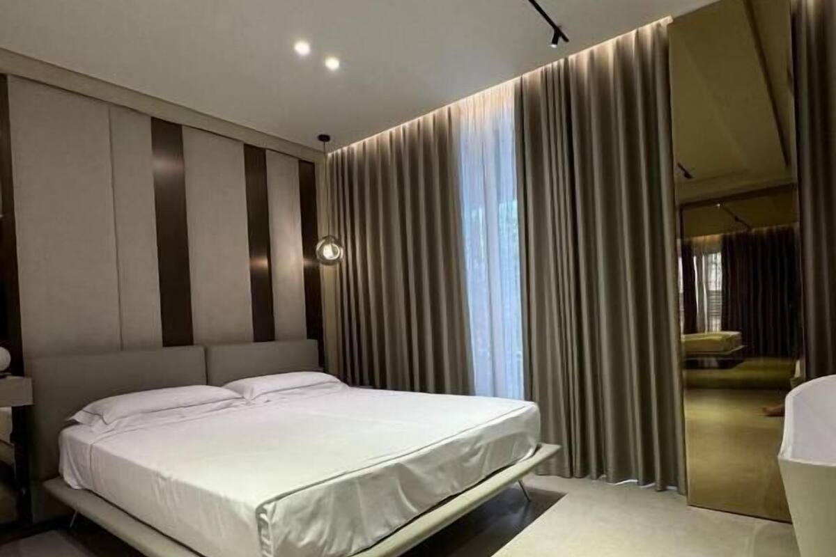 Quarto moderno com uma cama grande, uma mesinha de cabeceira e um espelho.