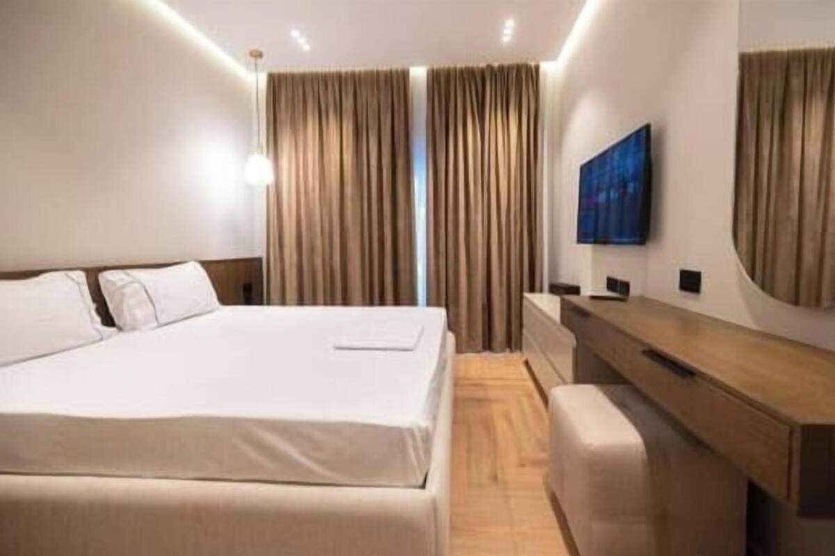 Quarto de hotel moderno com uma cama grande, escrivaninha de madeira, televisão de tela plana e um espelho amplo.