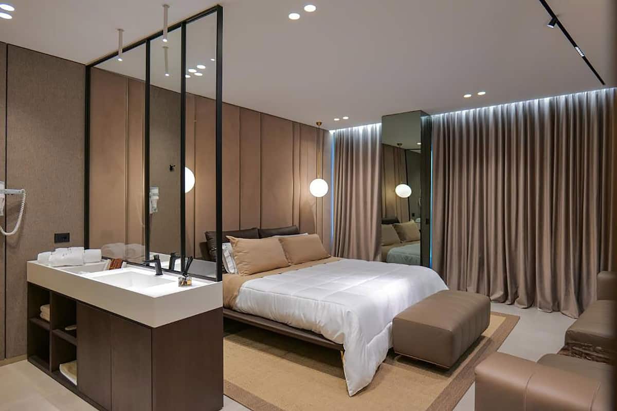 Quarto de hotel moderno com uma cama grande, banheiro separado com toucador e um espelho amplo.