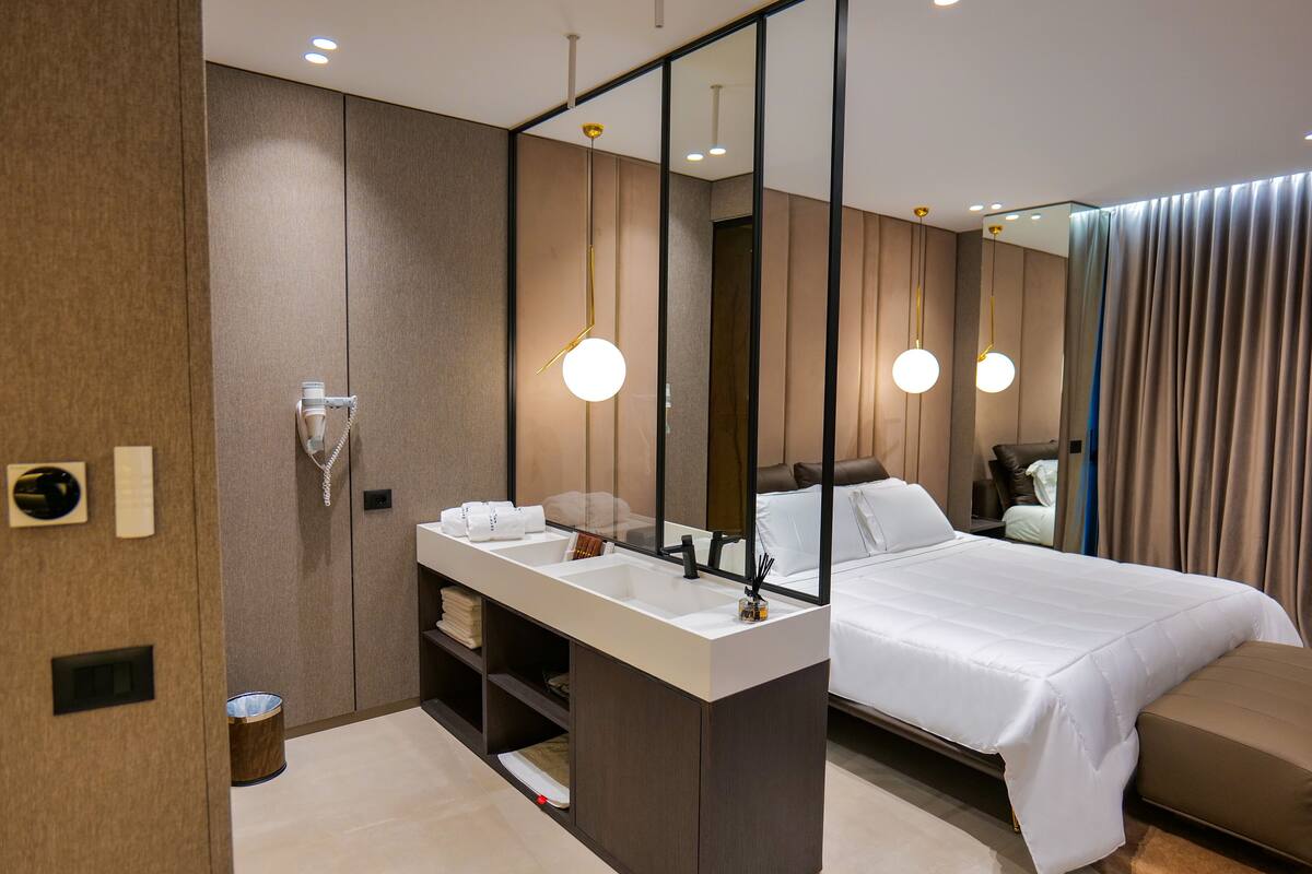 Quarto de hotel moderno com uma cama grande, toucador com espelho e área de chuveiro separada.