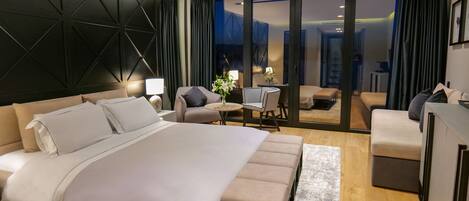 A modern hotel room with a large bed, a desk, a chair, and a sofa.