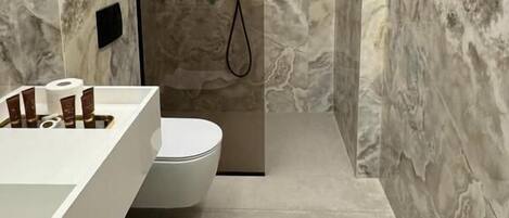 Un baño moderno con pared de mármol, un lavabo blanco y una zona de ducha.