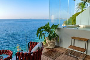 Un balcón con vista al mar, una silla, una mesita y una planta en maceta.