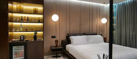 A modern hotel room with a large bed, a minibar, and a glass-enclosed refrigerator.