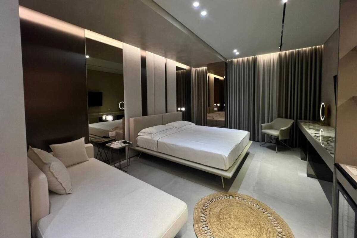 Quarto de hotel moderno com uma cama grande, um sofá, uma escrivaninha e um espelho.
