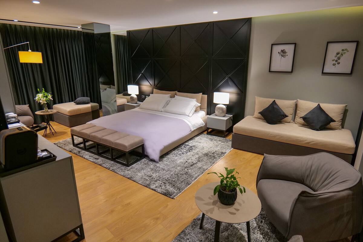 Quarto moderno com uma cama grande, mesas de cabeceira, um sofá, uma escrivaninha e uma cadeira.