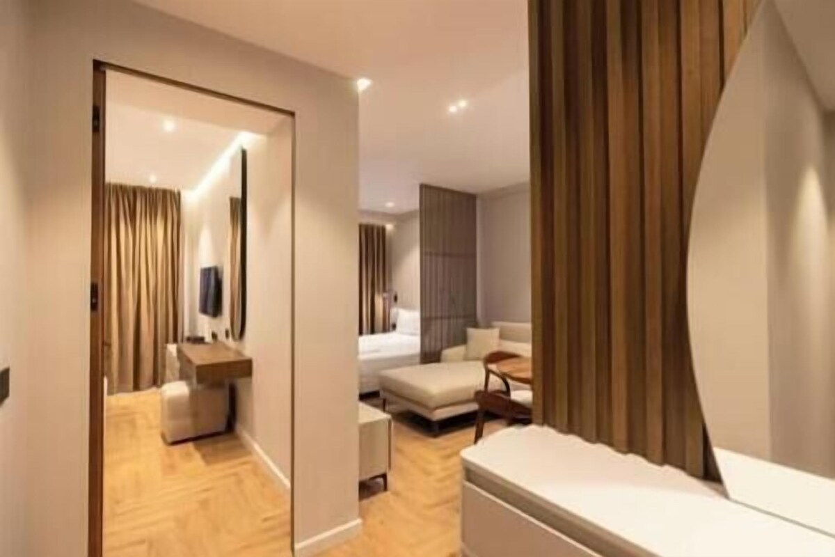 A modern hotel room with a wooden floor, a sofa, a bed, a desk, and a mirror.