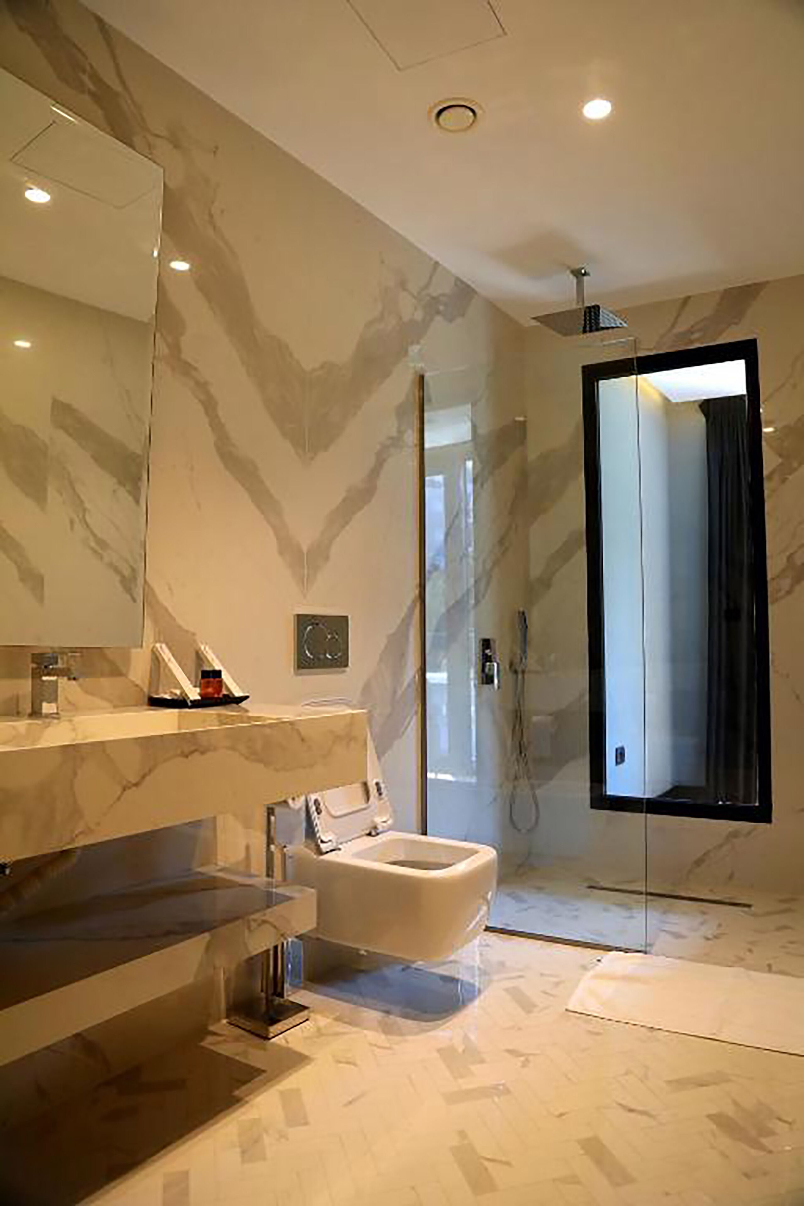 Une salle de bain moderne avec un meuble-lavabo en marbre, un grand miroir et une douche séparée par des parois en verre.