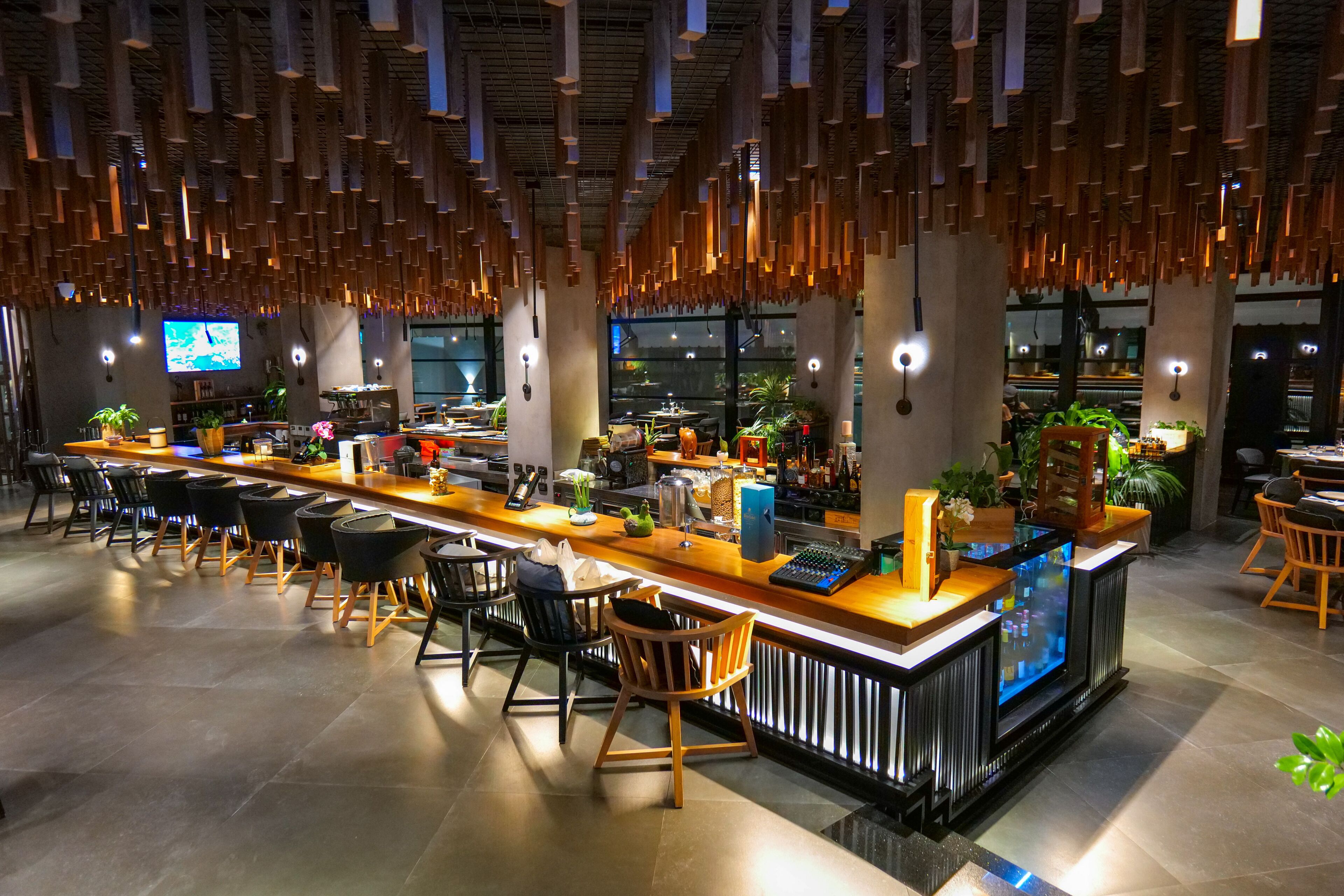 A modern bar area with wooden chairs, a counter with bar tools, and a television screen.