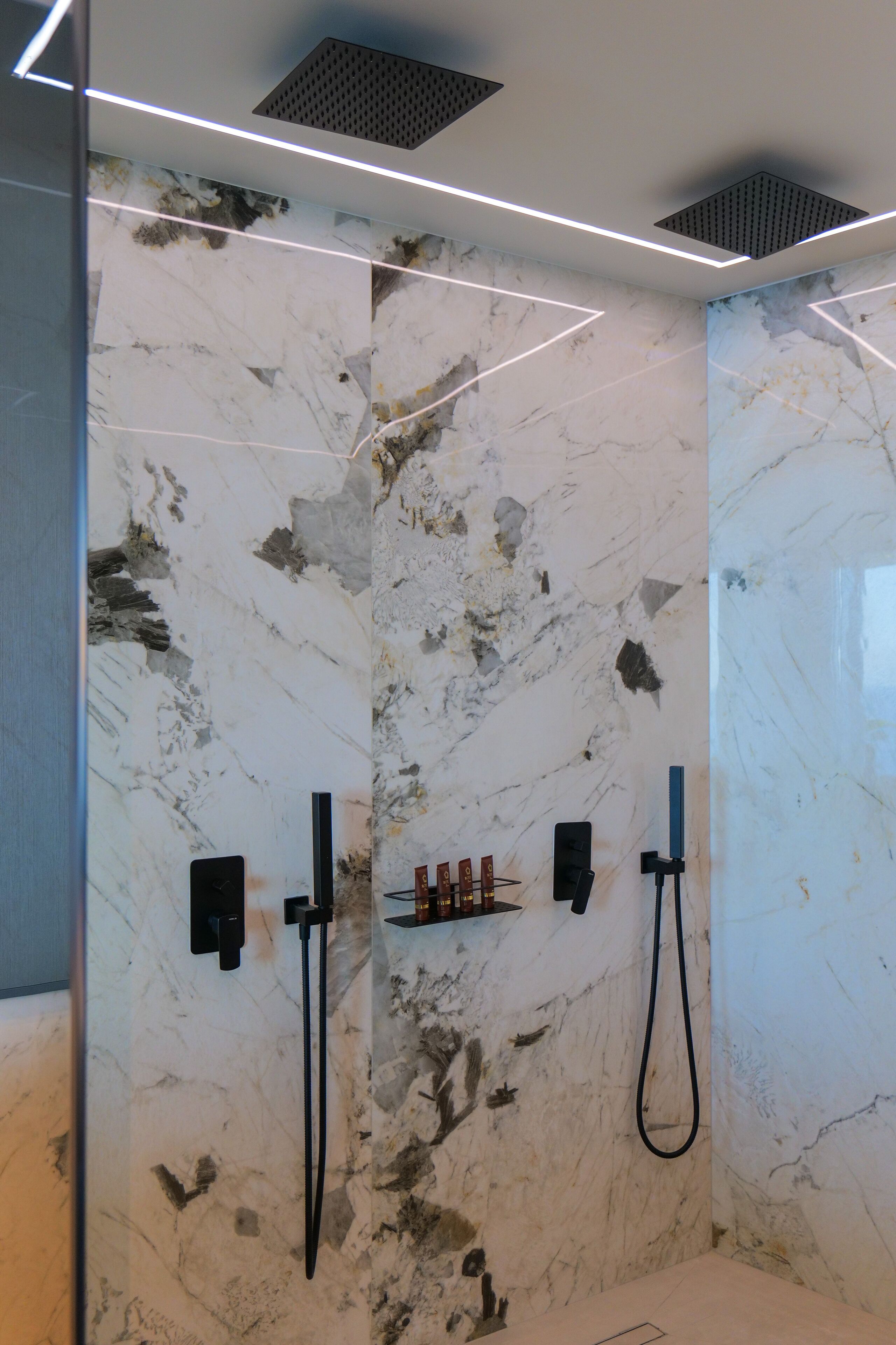 A modern bathroom with marble walls, a glass shower enclosure, and built-in towel racks.