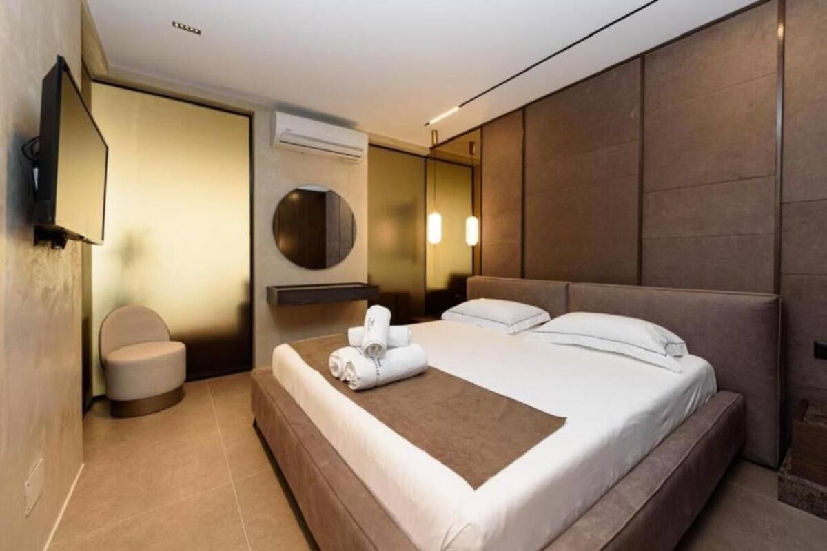 Una habitación de hotel moderna con una cama grande, un espejo redondo, un pequeño rincón de descanso y un televisor de pantalla plana montado en la pared.